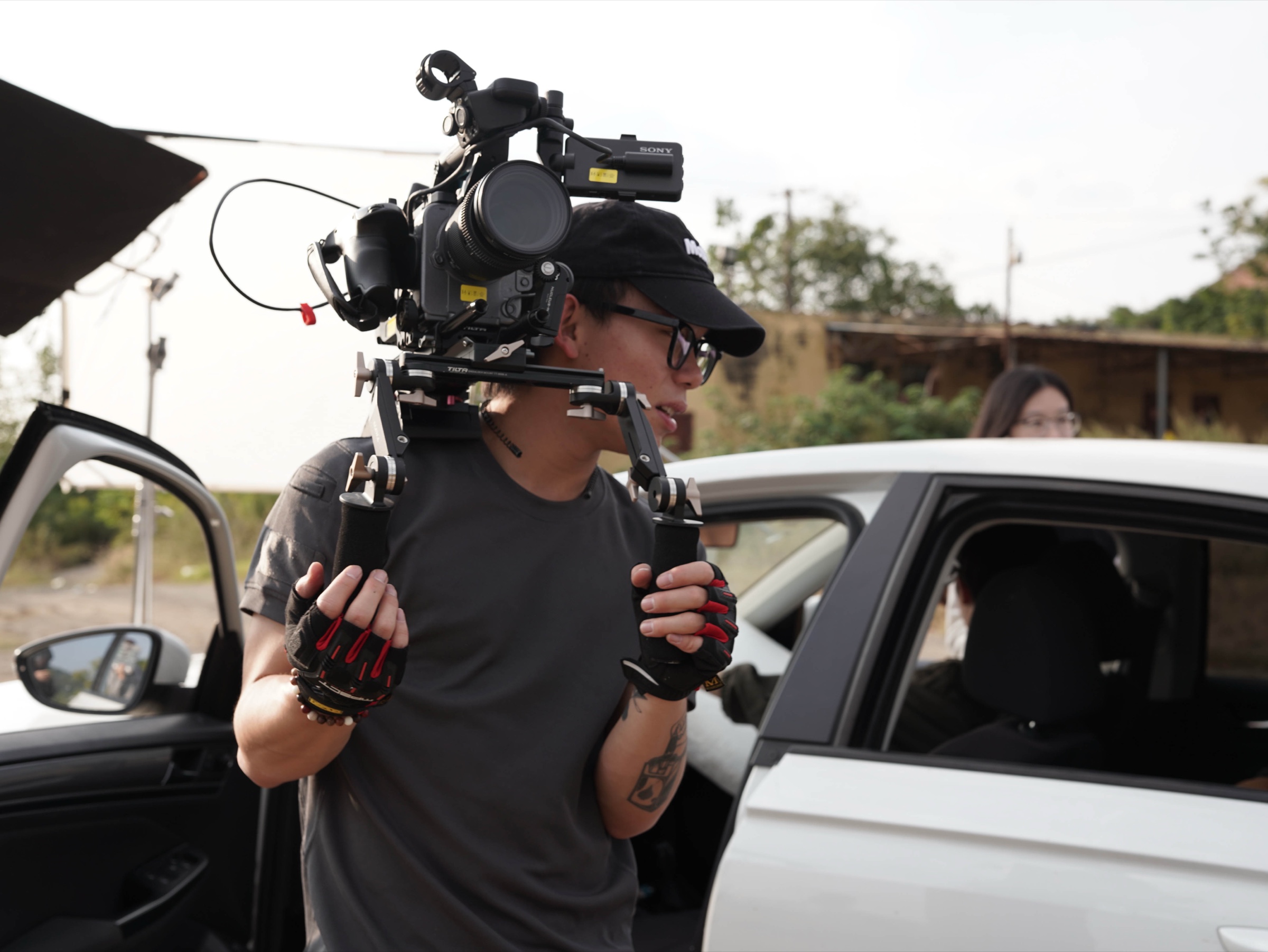 Jason Chen operating a shoulder-mounted cinema camera beside a car